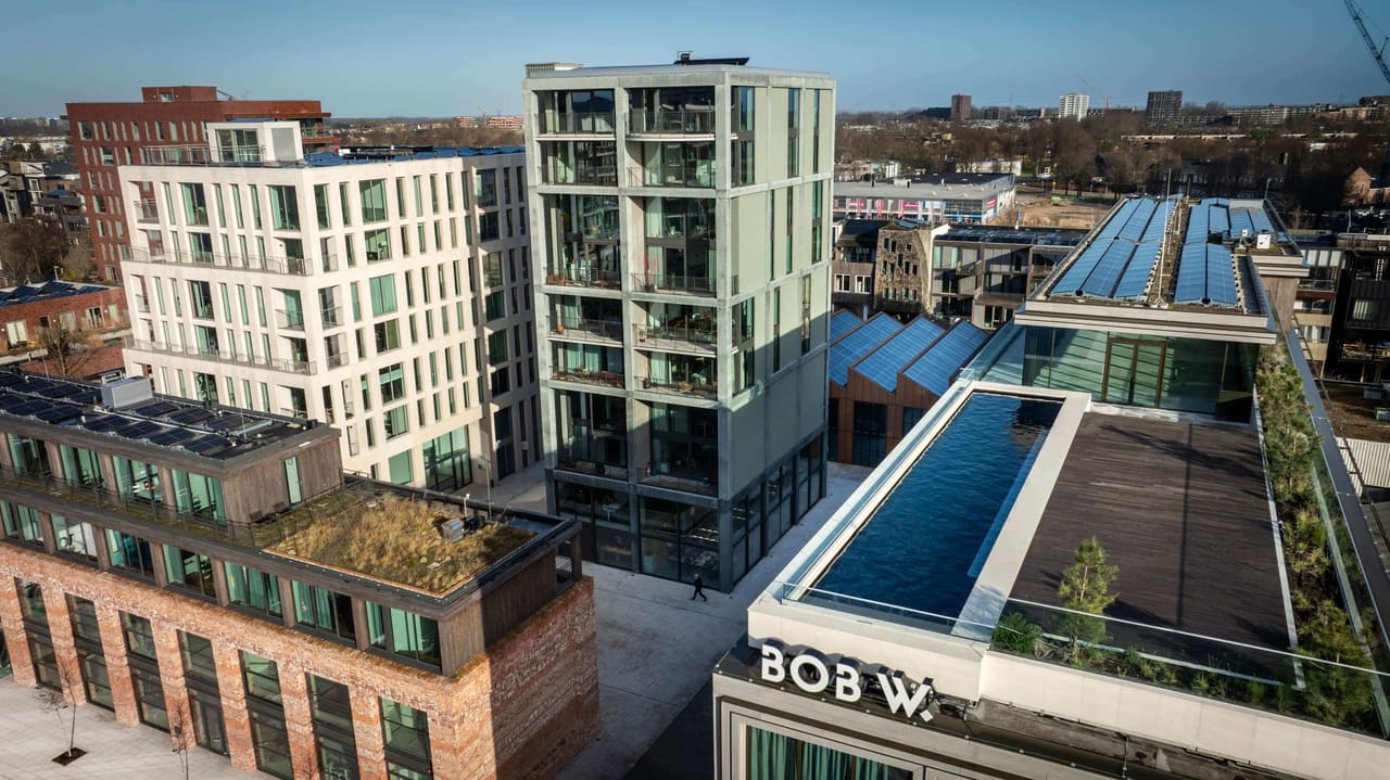 Aerial view of Republica in Amsterdam-Noord: the green concrete Superlofts tower, a white residential block, recycled-brick buildings and a rooftop pool