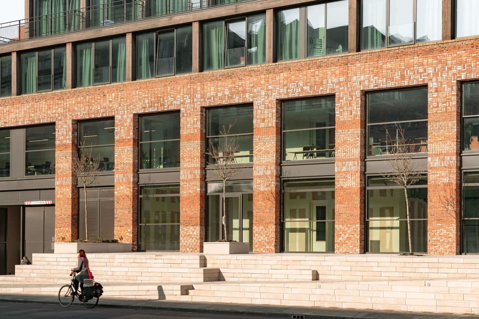 The recycled-brick restaurant building with wide seating steps facing south onto the stone square