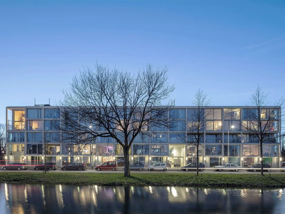 Superlofts Blok Y at dusk: a white concrete grid facade with lit lofts reflected in the canal